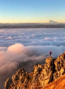 Pessoa em pico de montanha sobre mar de nuvens ao nascer do sol