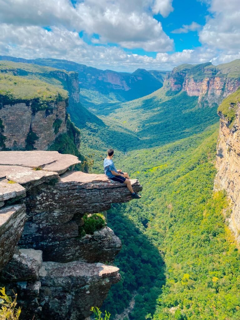 Aventureiro em penhasco contemplando vale verde na Chapada Diamantina