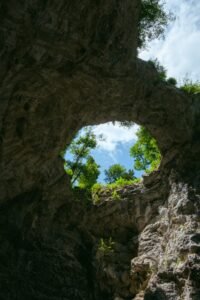 Céu e árvores vistos por abertura no teto de caverna