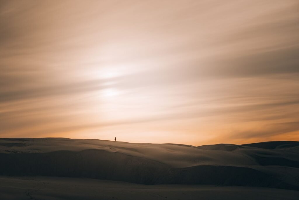 Pessoa solitária caminhando em dunas ao pôr do sol
