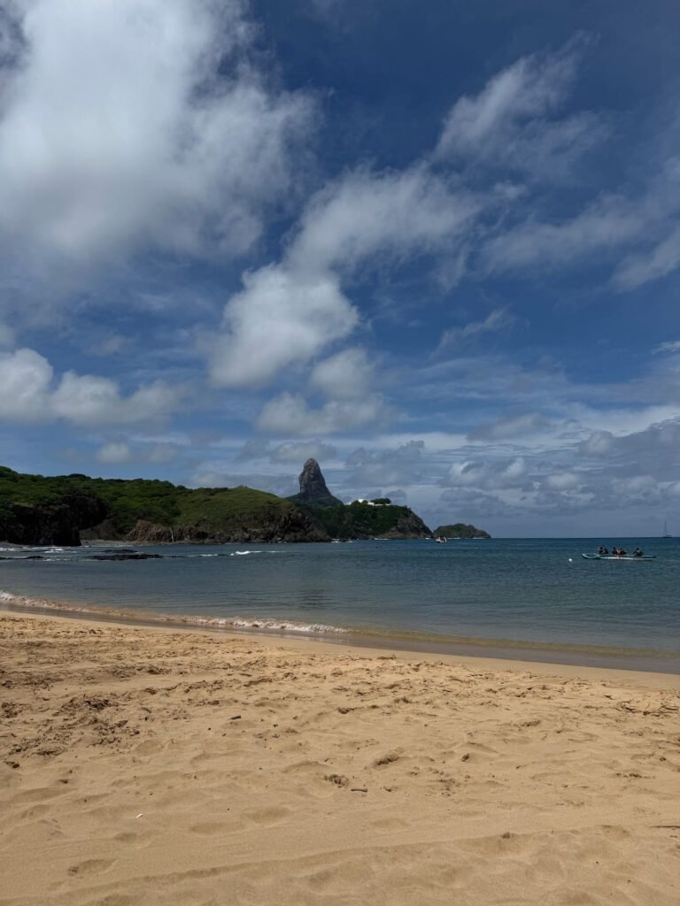 Praia de areia clara com morros verdes e mar calmo em Fernando de Noronha