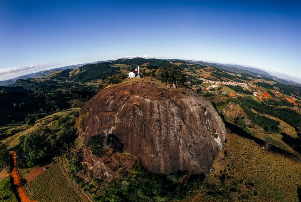 Igreja pequena com cruzeiro em penhasco cercado de mata