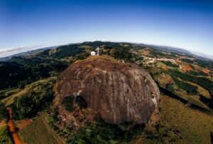 Igreja pequena com cruzeiro em penhasco cercado de mata
