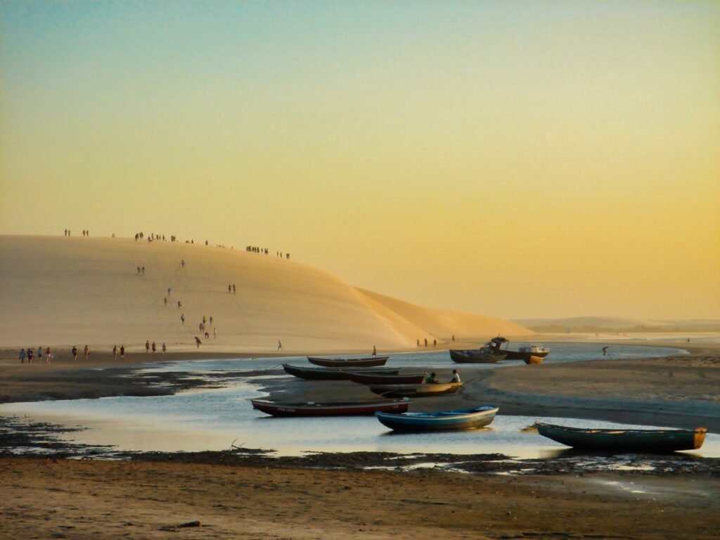 Barcos na areia da praia de Jericoacoara com a grande duna ao fundo durante o pôr do sol