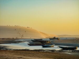 Barcos na areia da praia de Jericoacoara com a grande duna ao fundo durante o pôr do sol