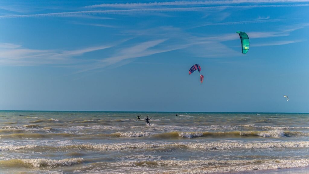 Kitesurfistas com kites coloridos voando sobre ondas do mar em dia de sol