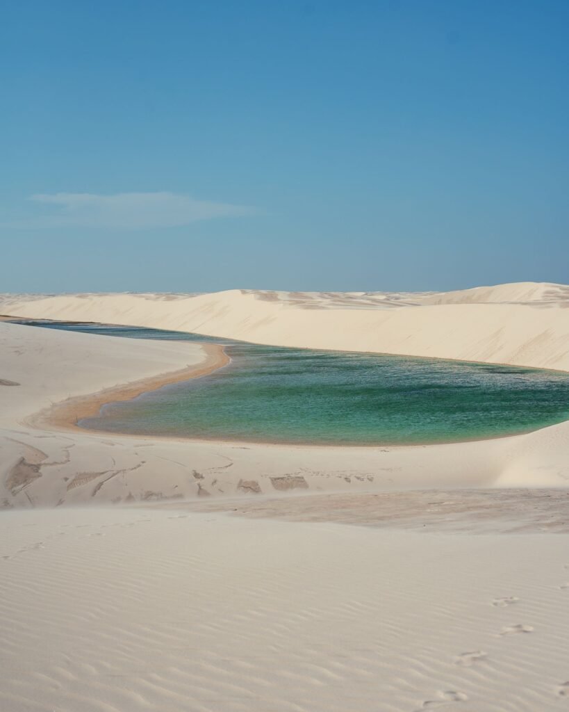 Lagoa de água azul cercada por dunas de areia branca nos Lençóis Maranhenses