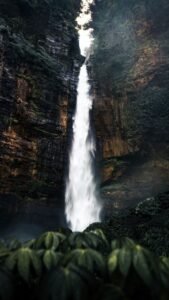 Cachoeira alta caindo entre vegetação exuberante e formações rochosas