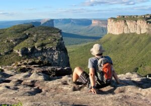 Trilheiro contemplando formações rochosas avermelhadas em paisagem seca