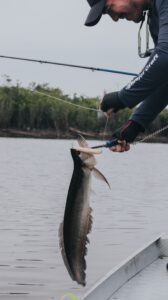 Pescador com vara em barco em rio de água escura