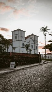 Igreja branca histórica com rua de pedras ao pôr do sol em cidade colonial