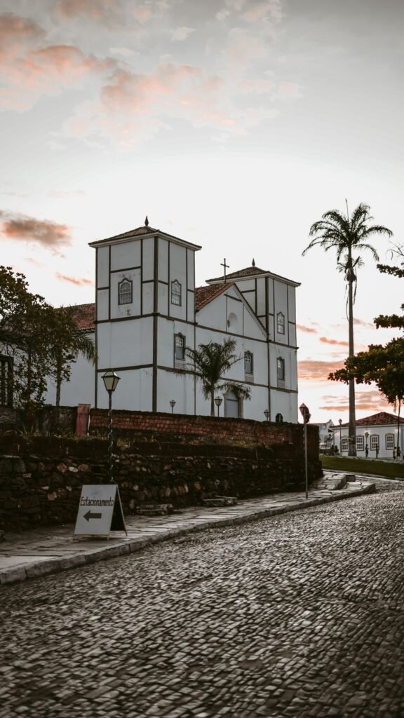Igreja branca histórica com rua de pedras ao pôr do sol em cidade colonial
