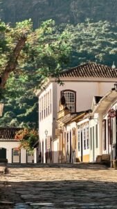 Rua de pedra colonial ensolarada com casario e vegetação