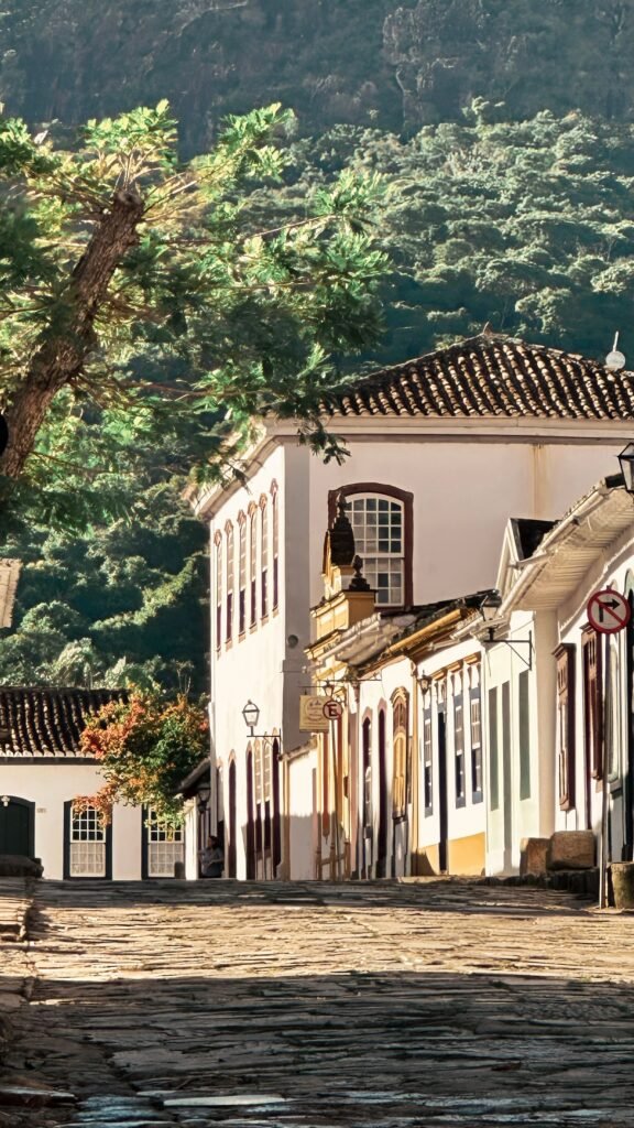Rua de pedra colonial ensolarada com casario e vegetação