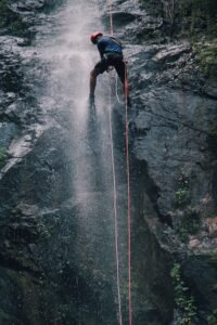 Aventureiro descendo de rapel ao lado de uma cachoeira alta