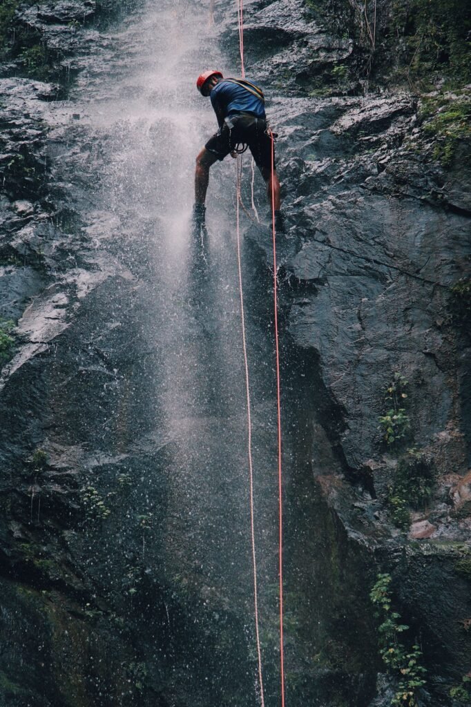 Aventureiro descendo de rapel ao lado de uma cachoeira alta
