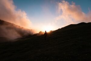 Silhueta de trilheiro ao amanhecer em colina com névoa
