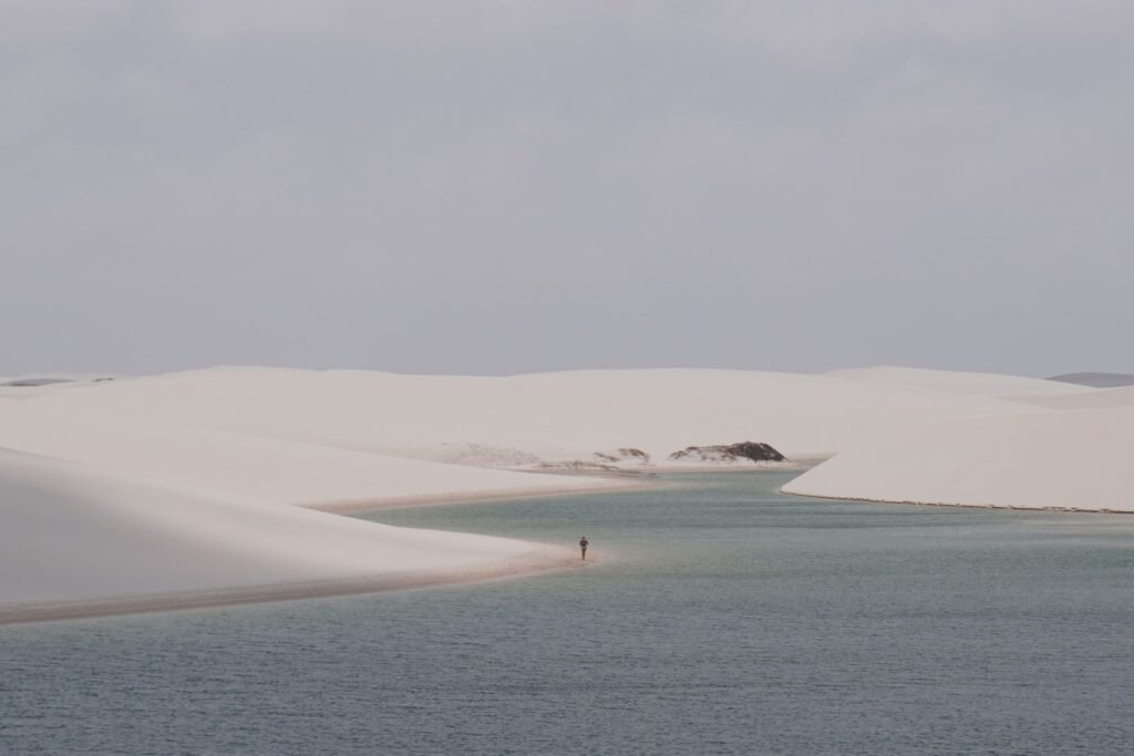 Pessoa caminhando pelas dunas com lagoas ao fundo na região de Atins