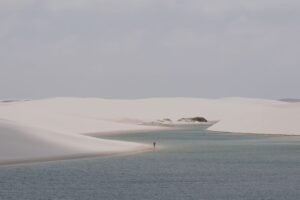 Pessoa caminhando pelas dunas com lagoas ao fundo na região de Atins